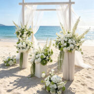Green and white artificial hydrangea wedding centerpieces on pedestals at a beach ceremony
