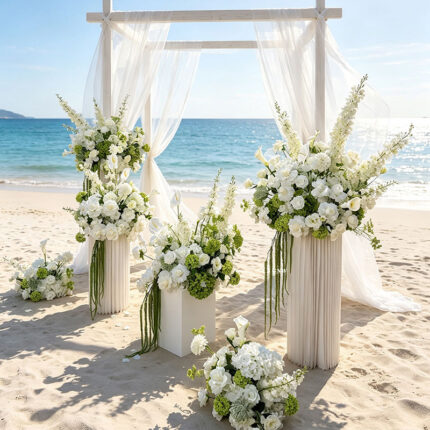 Green and white artificial hydrangea wedding centerpieces on pedestals at a beach ceremony