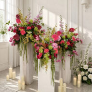 Pink faux wedding flower arrangements with trailing greenery on tall display stands
